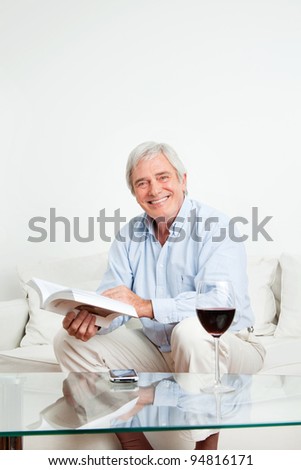 Happy senior man reading a bestseller book on couch