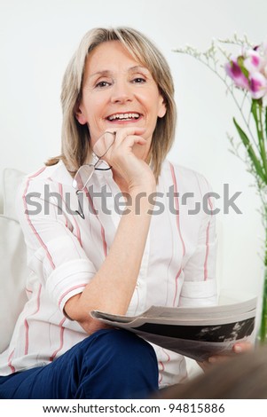 Happy senior woman with newspaper and glasses in living room