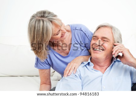 Happy senior couple talking in cell phone at home
