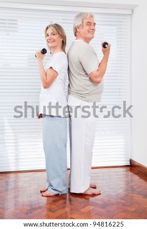 Happy senior couple doing dumbbell fitness exercises in gym