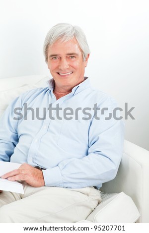 Elderly relaxed man reading a book on couch in living room