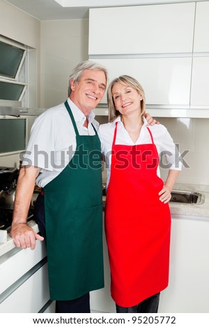 Two happy senior people with aprons in the kitchen