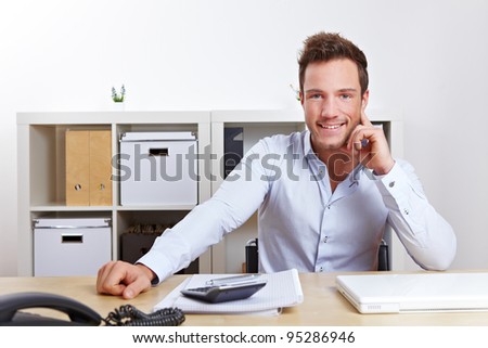 Happy young business man sitting at desk in office