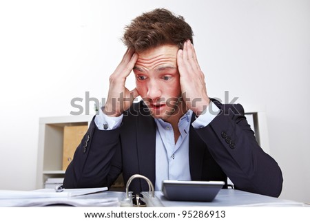 Shocked young business man in office looking at files