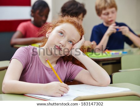 Pensive girl in elementary school class thinking and writing