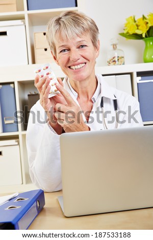 Smiling elderly doctor recommending pills at desk in office