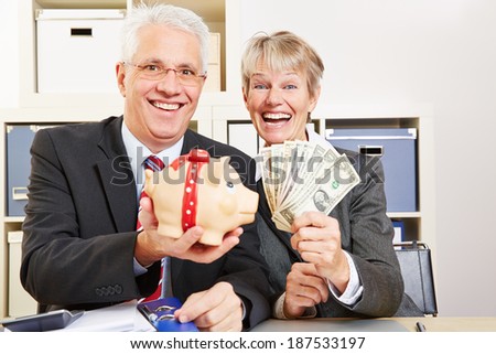 Two elderly happy business people with fan of dollar bills and piggy bank