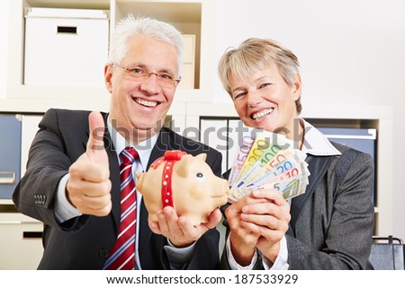 Two happy senior people with money and piggy bank holding thumb up