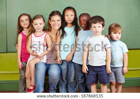 Happy group of children with smiling kindergarten teacher in a room