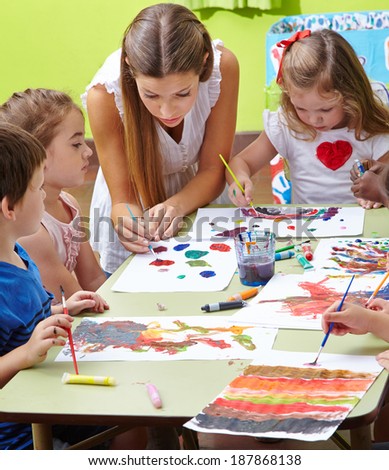 Nursery teacher painting with children and brushes and watercolor in kindergarten