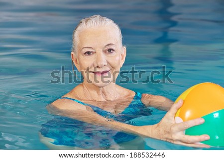 Happy senior woman with water ball in swimming pool doing aqua fitness