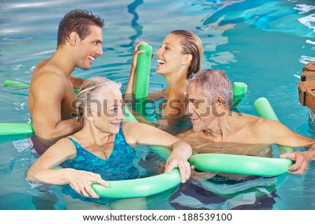 Happy group in swimming pool doing aqua fitness with swim noodles