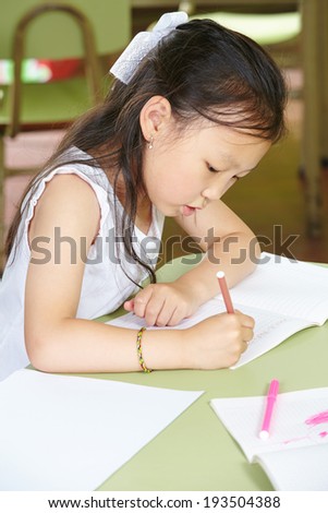 Chinese girl learning to write in kindergarten with a pen at a table