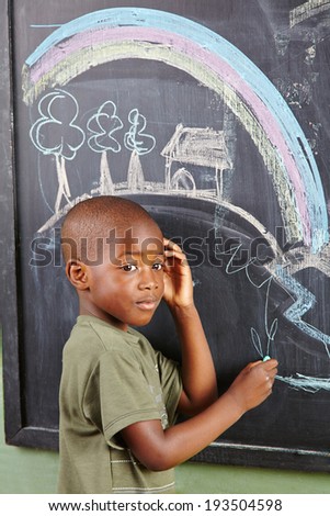 African boy drawing colorful picture on a blackboard in kindergarten
