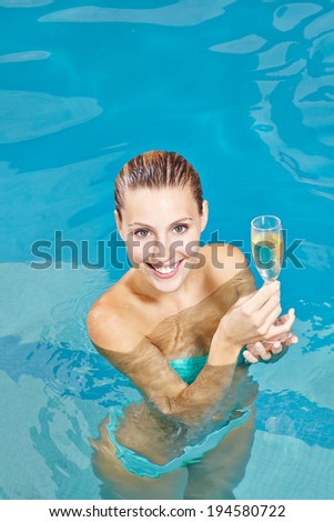 Happy young woman drinking champagne in swimming pool of hotel