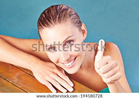 Happy smiling woman in water of swimming pool holding her thumbs up