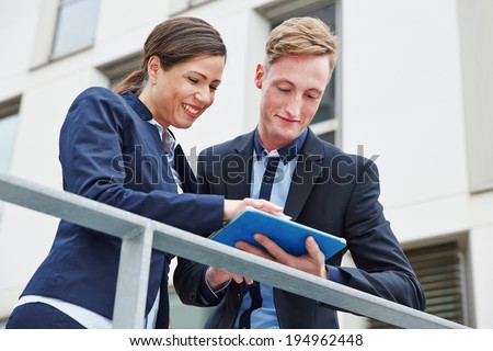 Two happy business people working with tablet computer outside in the city