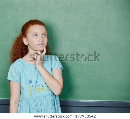 Girl thinking at chalkboard in elementary school class