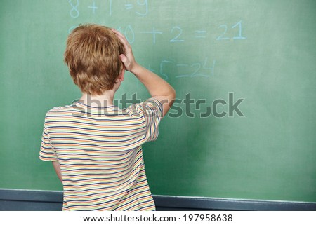 Child standing in class in front of chalkboard and thinking about solution
