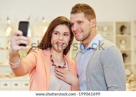 Happy couple taking a selfie photo with smartphone in a jewelry store