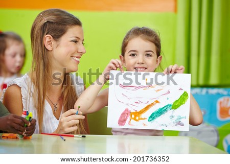 Girl showing self drawn painting in kindergarten with nursery teacher