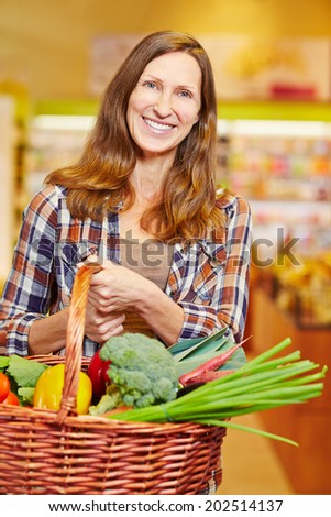 Attractive elderly woman carrying shopping basket full of fresh vegetables