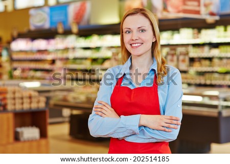 Young happy saleswoman with red apron in a supermarket
