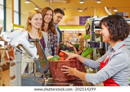 Young woman paying basket of groceries at supermarket checkout