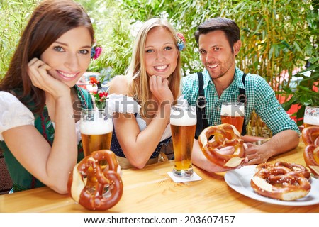 Happy friends sitting in beer garden in Bavaria with pretzel