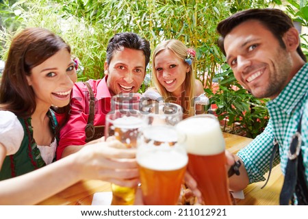 Smiling friends in beer garden clinking their glasses in summer