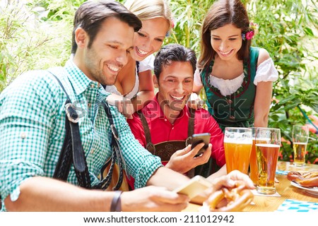 Happy friends in beer garden looking together at smartphones