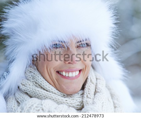 Smiling woman with white fur cap in winter snow