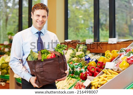 Smiling businessman buying bag of fresh vegetables in organic food store