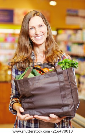 Attractive smiling woman in supermarket holding shopping bag full of vegetables