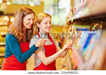 Young retal saleswoman trainee in supermarket getting help from staff