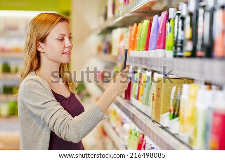 Young woman comparing prices with a smartphone app in a drugstore