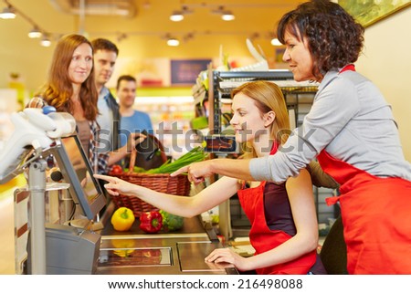 Elderly saleswoman helping young woman at supermarket checkout