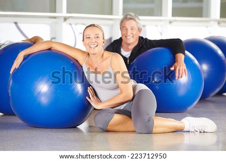 Two happy senior people sitting in gym with exercise ball