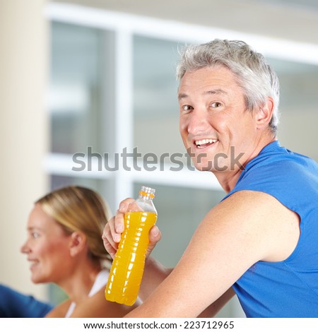 Elderly man drinking isotonic sports drink in a gym