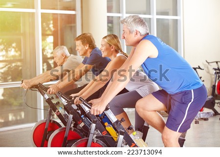 Happy group in gym exercising on bikes in summer