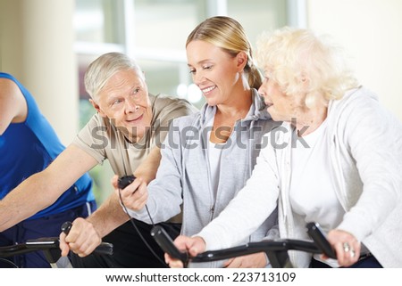 Fitness trainer measuring time for senior people on bikes in gym