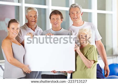 Group of happy senior people holding white empty cardboard sign in gym