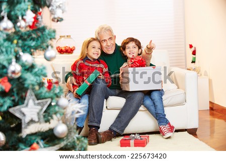 Two children sitting with gifts and grandfather at christmas on the sofa