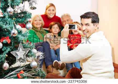 Smiling man taking family picture at christmas with his smartphone camera
