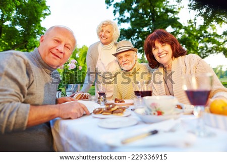 Happy senior people sitting at set coffee table in a summer garden