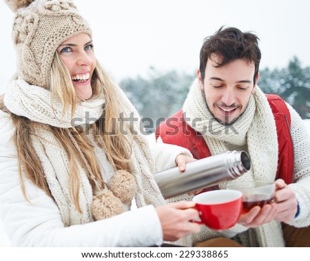 Happy woman pouring man tea from thermos jug in winter