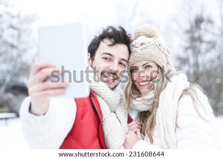 Happy couple in winter taking pictures of themselves with tablet PC