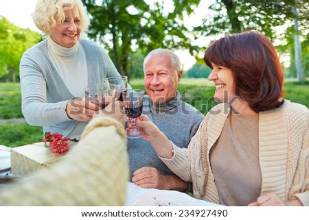 Happy senior friends cheering with glass of red wine at birthday party