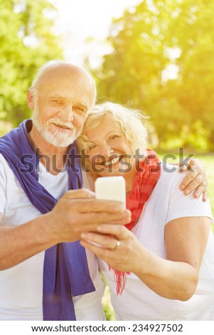 Happy senior couple taking a selfie with smartphone in a fall garden