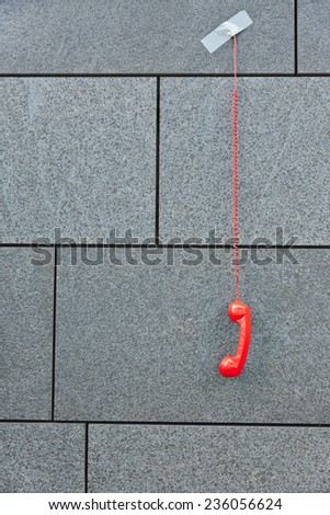 Red phone hanging down taped to a grey wall